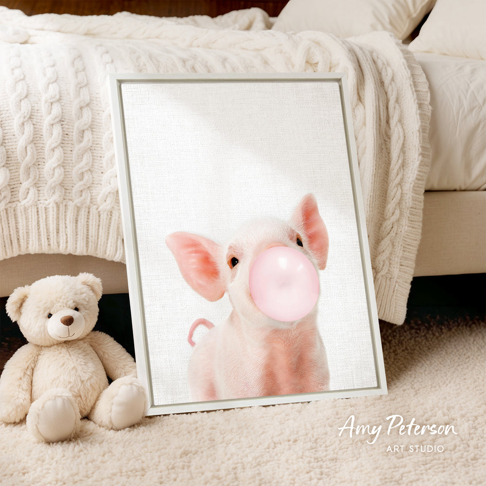 A framed image of a pig blowing a bubble gum bubble is displayed on a white bedspread, accompanied by a teddy bear.
