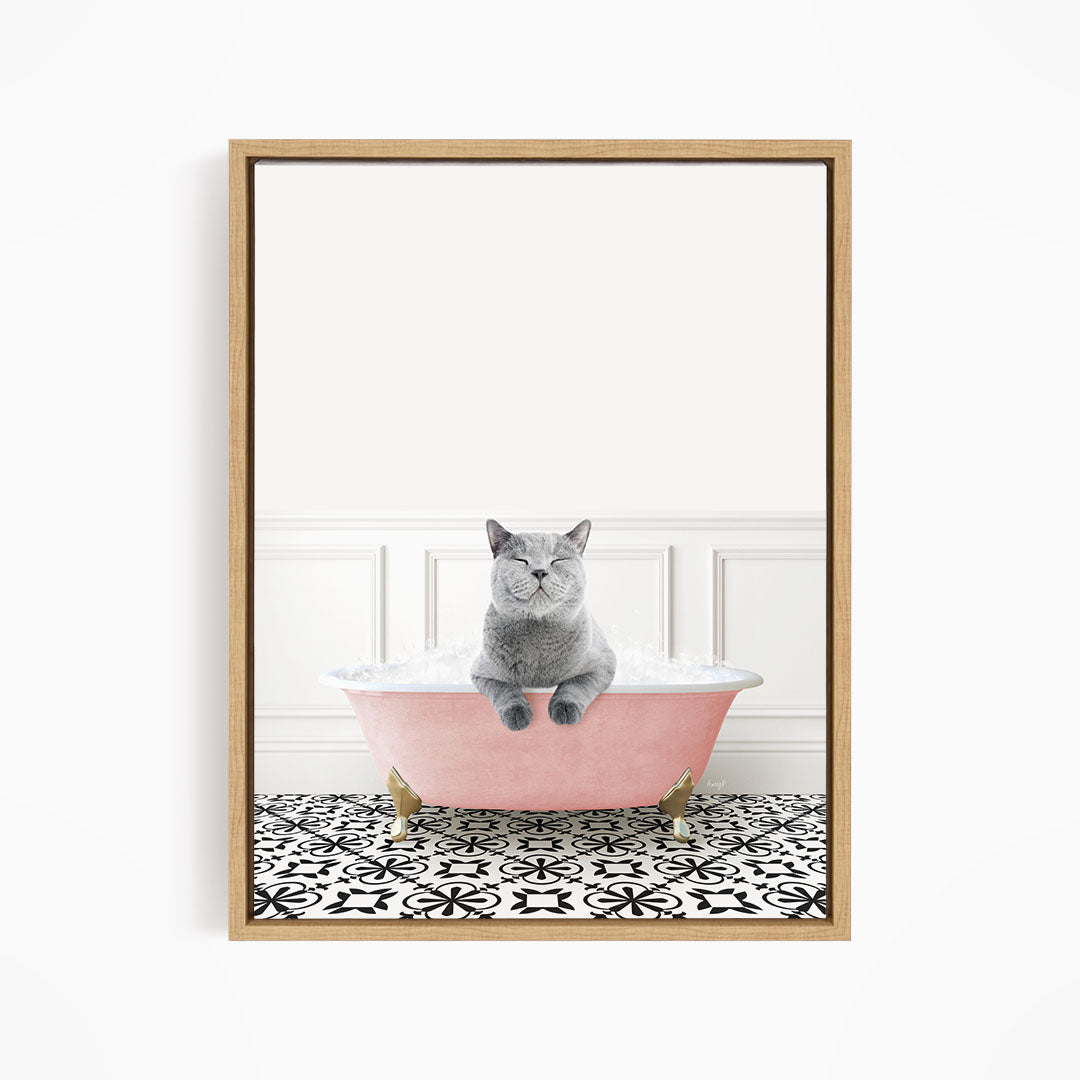 A gray cat sitting in a pink bathtub filled with bubbles, with a black and white patterned floor in the background.
