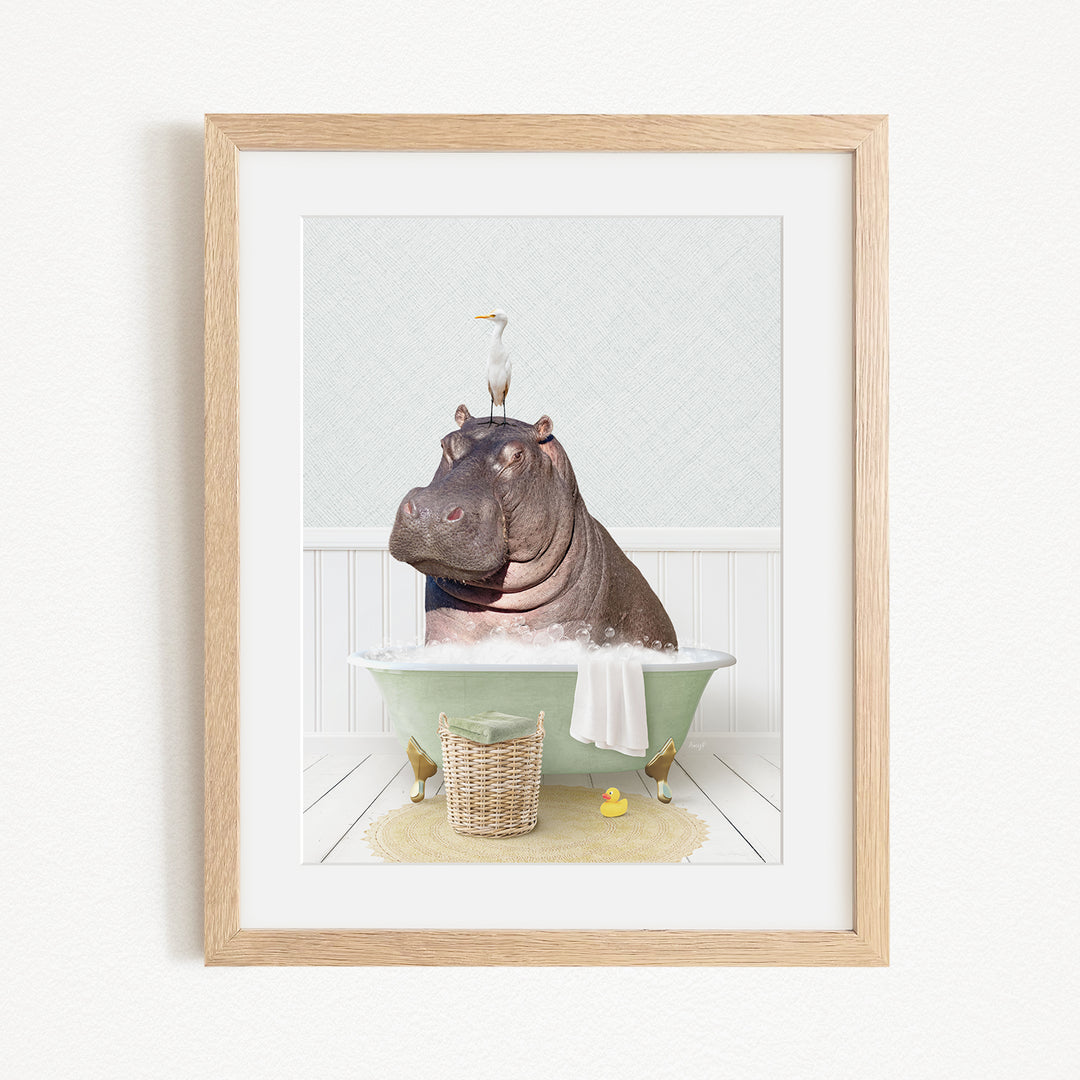 A framed image depicting a hippopotamus sitting in a bathtub, with a bird perched on its head.