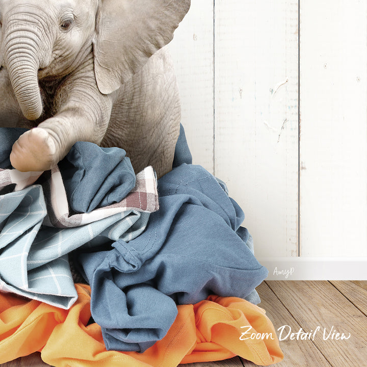 A baby elephant sitting on a pile of clothes, with a wooden wall in the background.