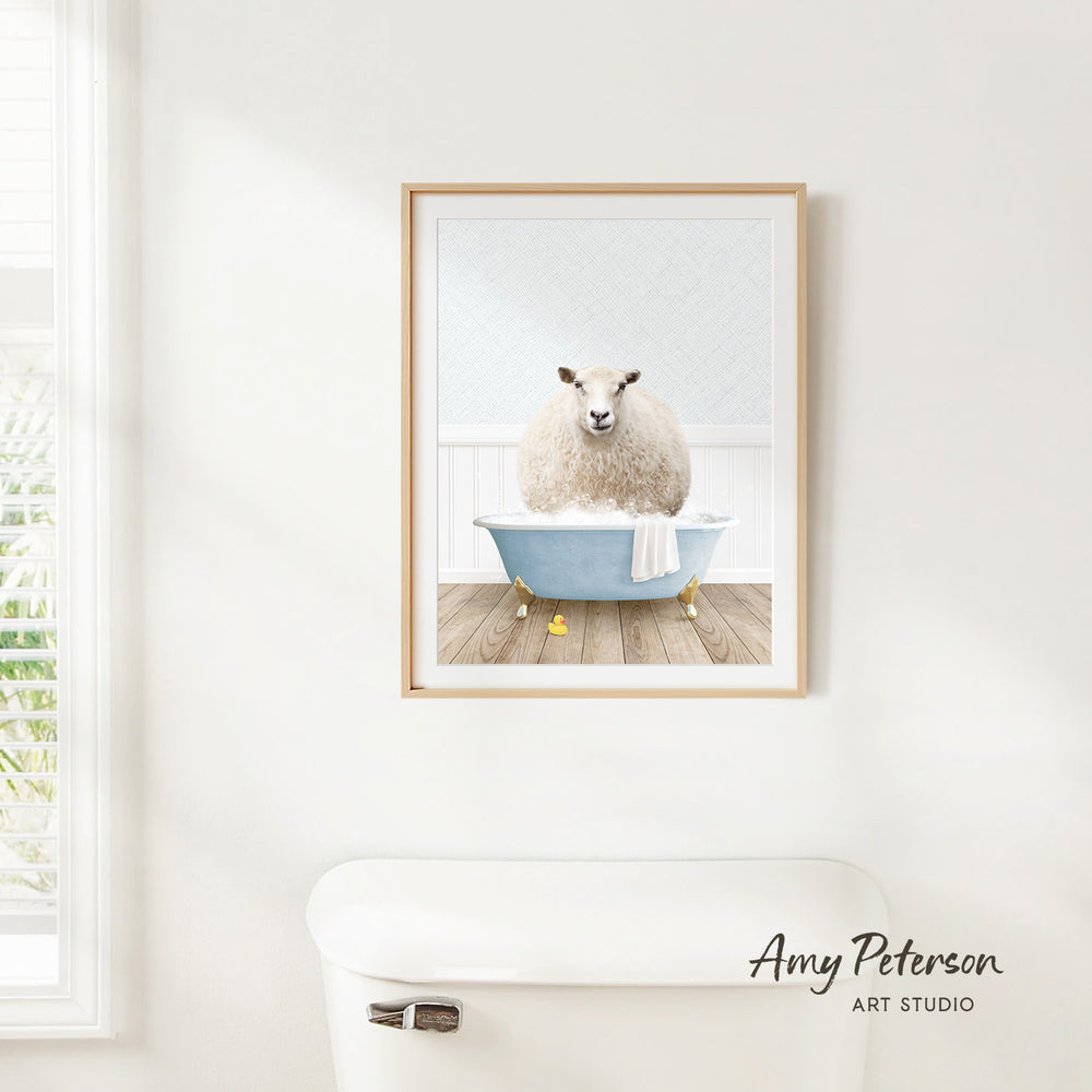 A framed print of a sheep sitting in a bathtub is hanging on a white wall in a bathroom.