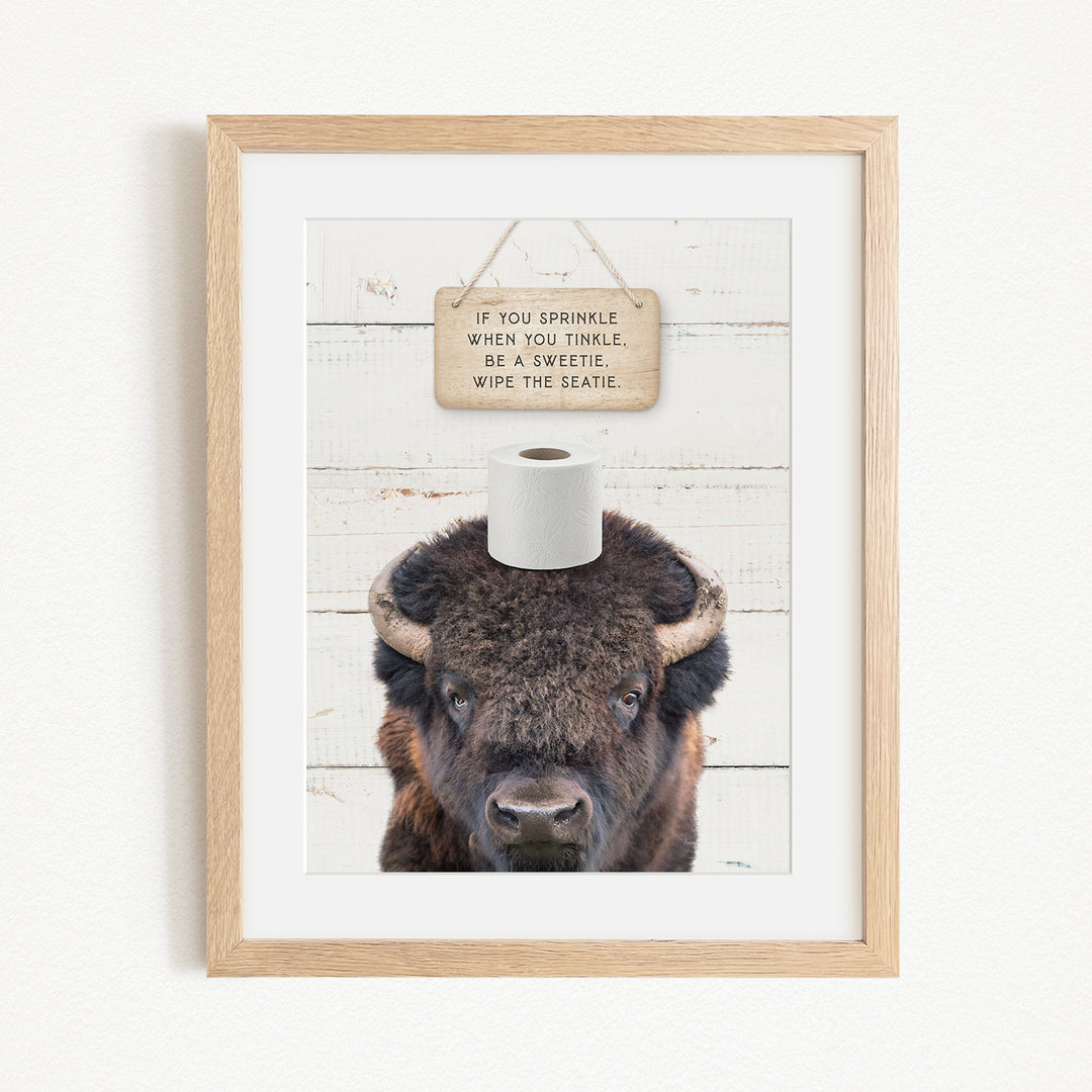 A framed image of a bison with a sign above it that reads "If you sprinkle when you tinkle, be a sweetie, wipe the seattle."