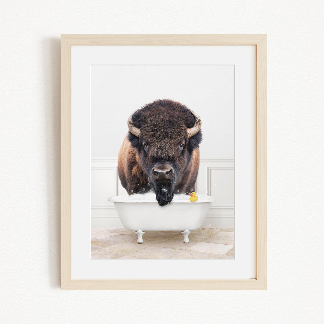 A buffalo with large horns is standing in a white bathtub, with a yellow rubber duck floating in the water.