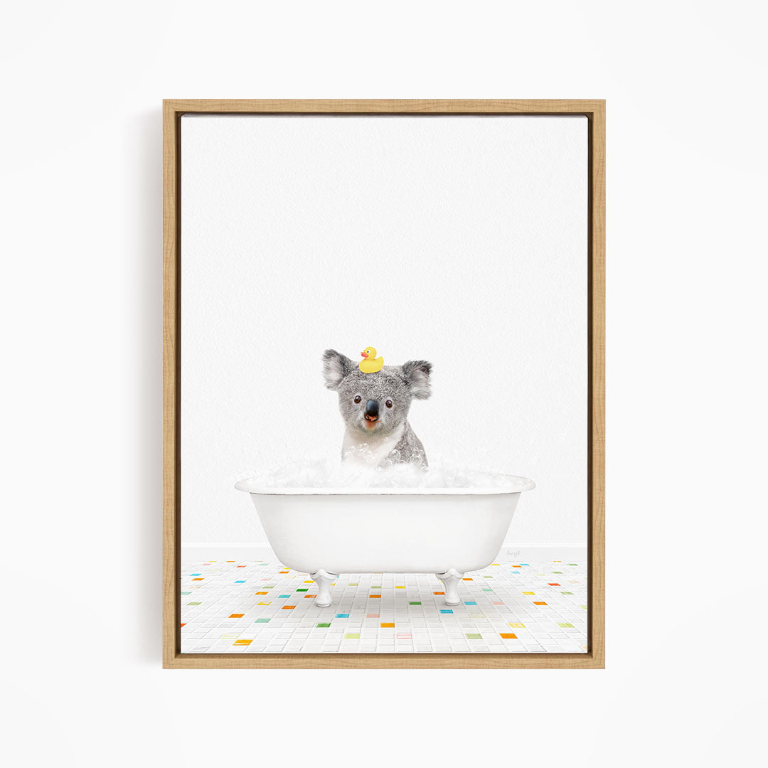 A koala bear sitting in a white bathtub filled with bubbles, with a rubber duck perched on its head.