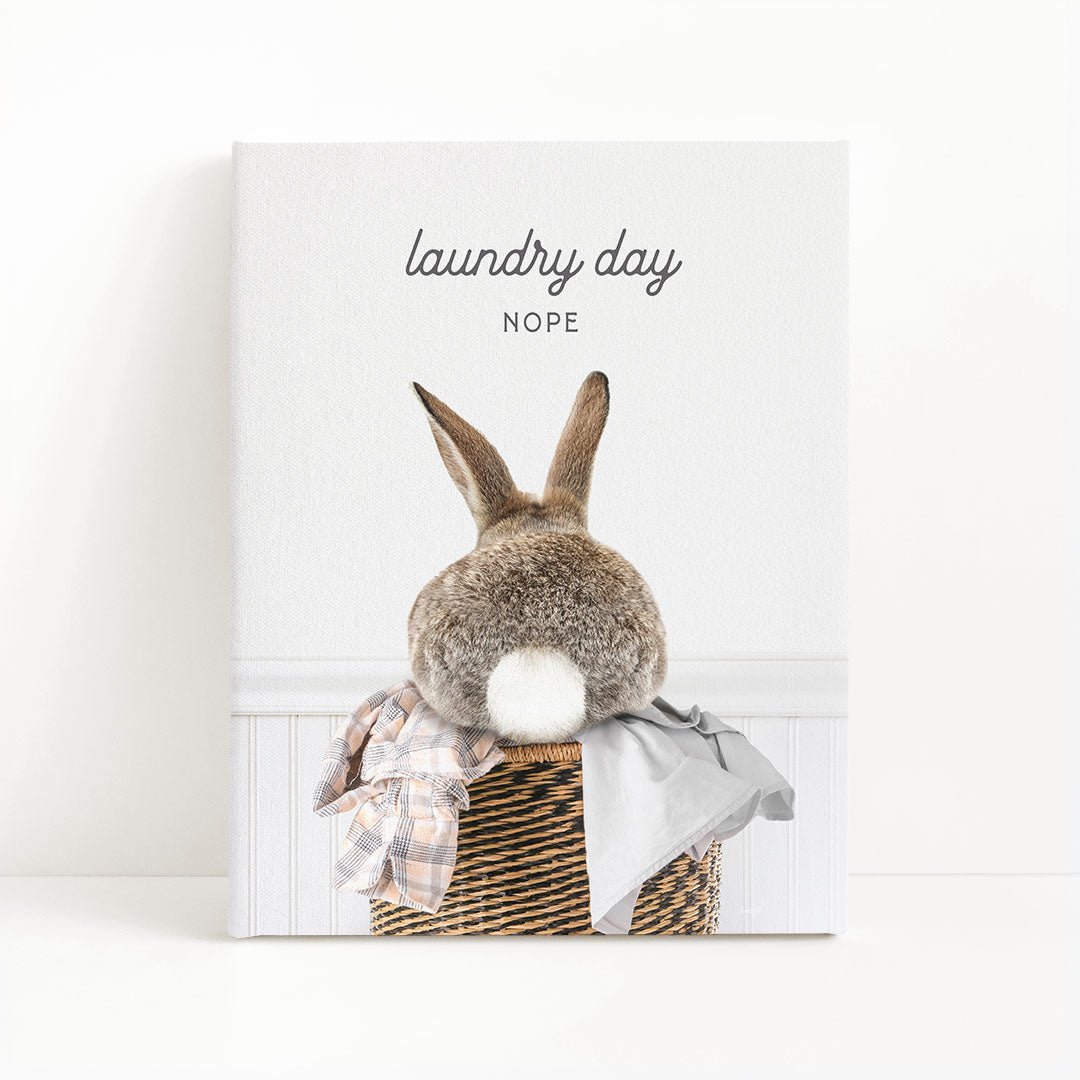 A rabbit sitting in a wicker basket filled with laundry, with the text "laundry day NOPE" above the image.