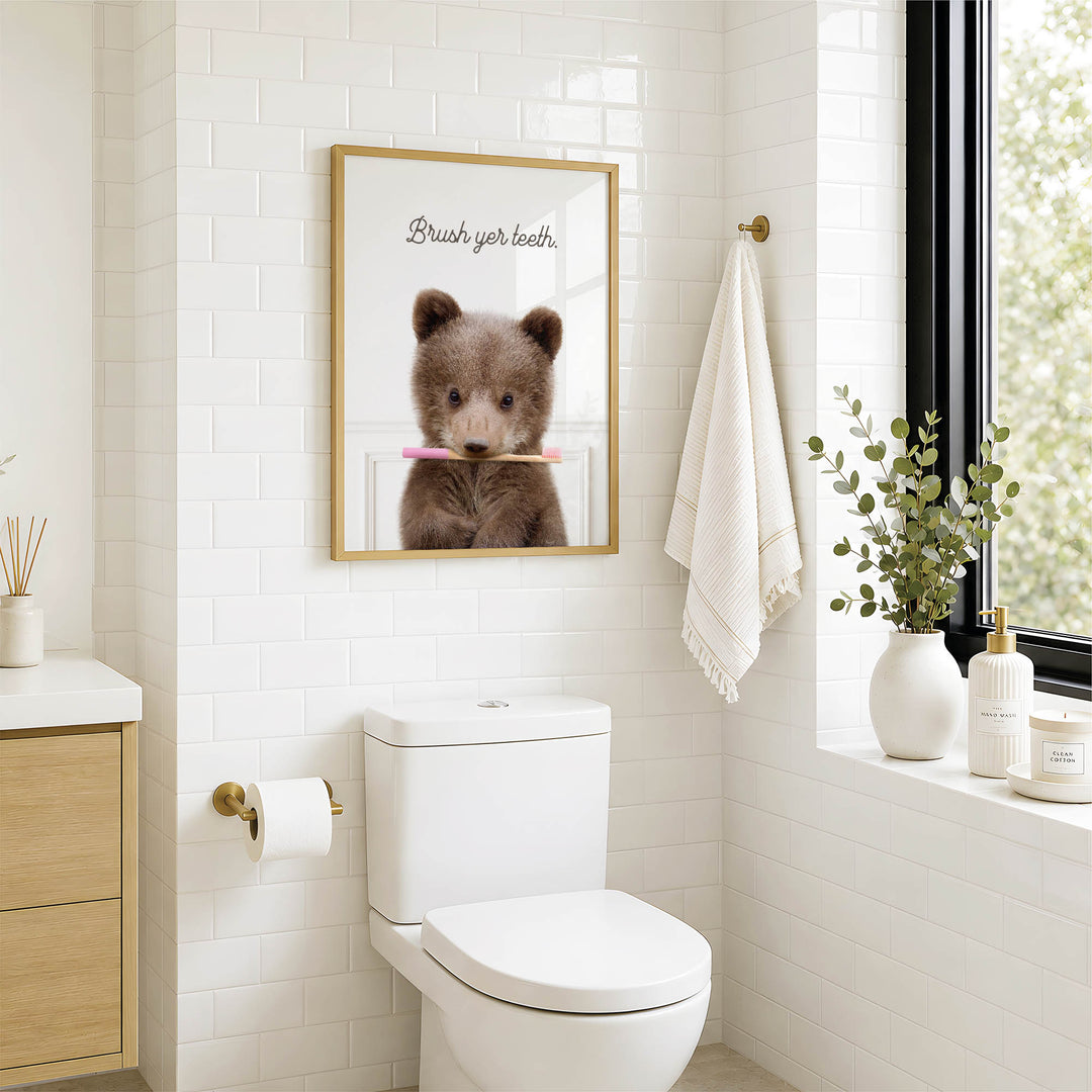 A bathroom with a white toilet, a framed image of a bear holding a toothbrush, and a towel hanging on a rack.