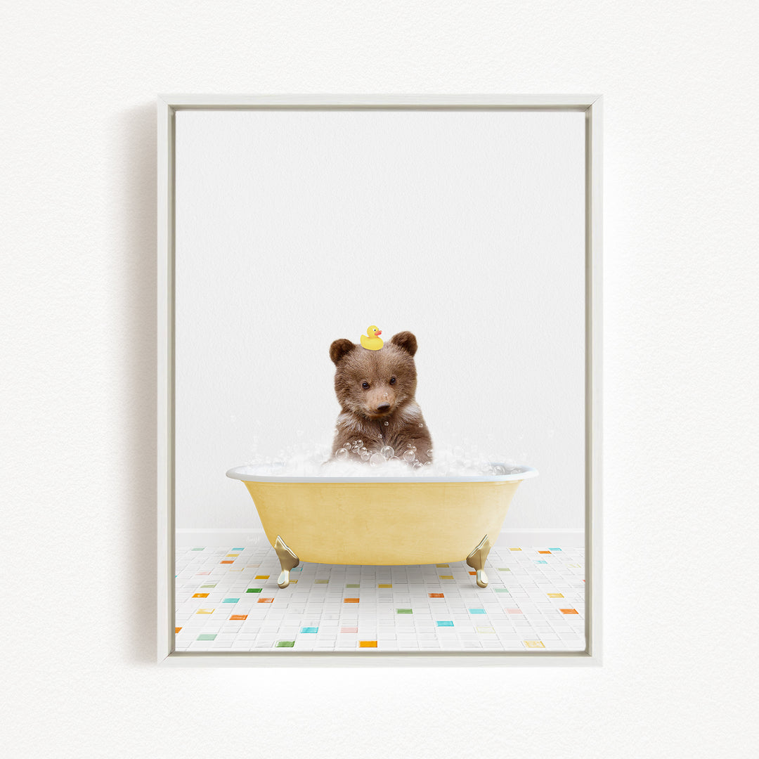 A brown bear sitting in a yellow bathtub filled with bubbles, with a rubber duck on its head.