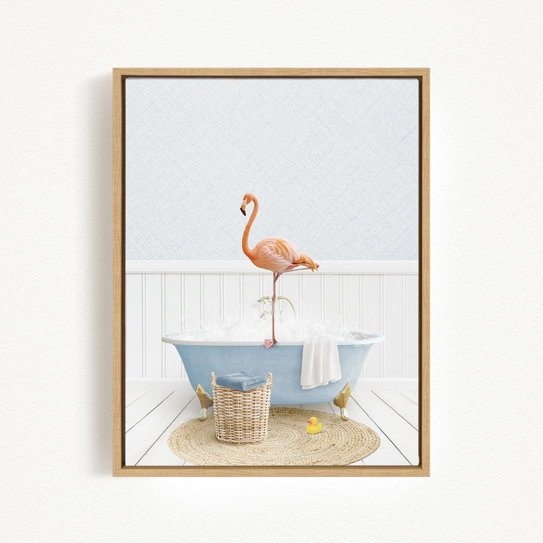 A framed image depicting a pink flamingo standing on a blue bathtub filled with bubbles, with a basket of bath toys and a yellow rubber duck nearby.