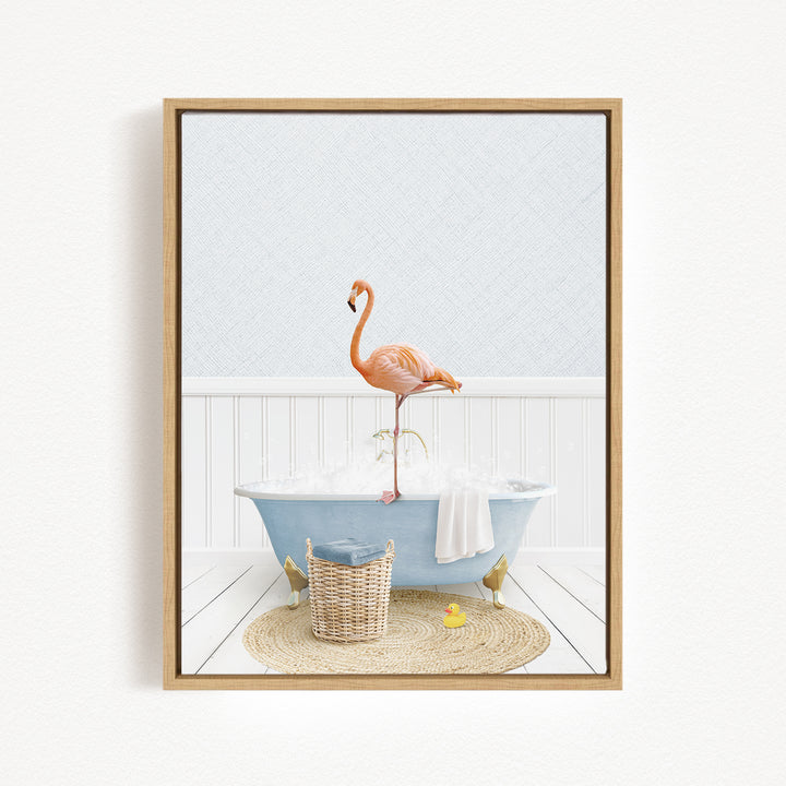 A framed image depicting a pink flamingo standing on a blue bathtub filled with bubbles, with a basket of bath toys and a yellow rubber duck nearby.