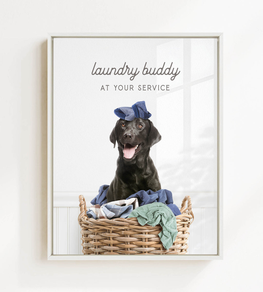 A black dog wearing a blue hat sits in a wicker laundry basket filled with clothes, with the text "laundry buddy at your service" displayed above the image.