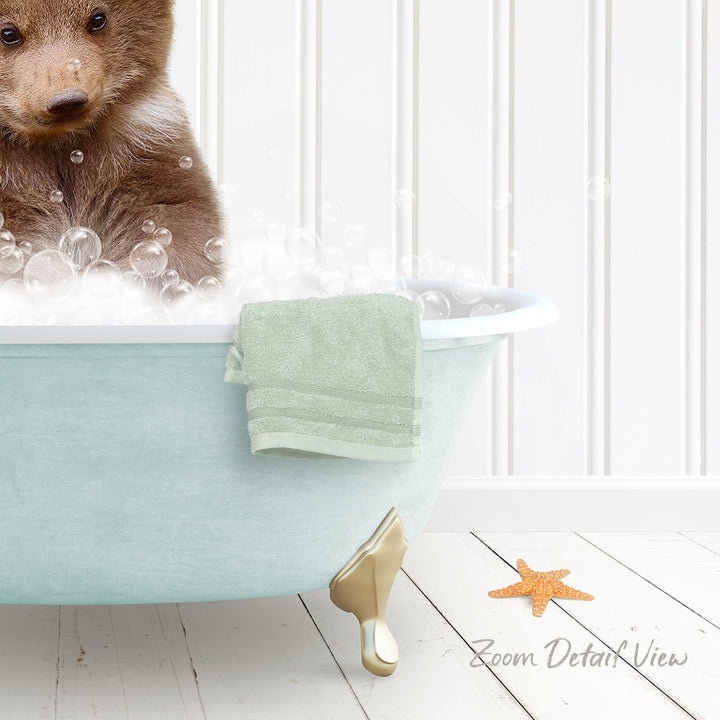 A brown bear is sitting in a light blue bathtub filled with bubbles, with a green towel and a starfish nearby.