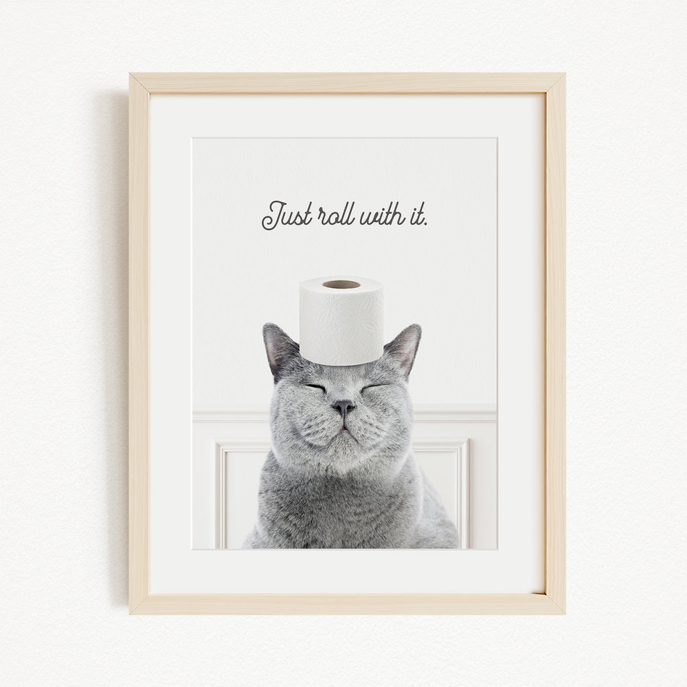 A gray cat with its eyes closed and a roll of toilet paper on its head, with the text "Just roll with it" above the cat.