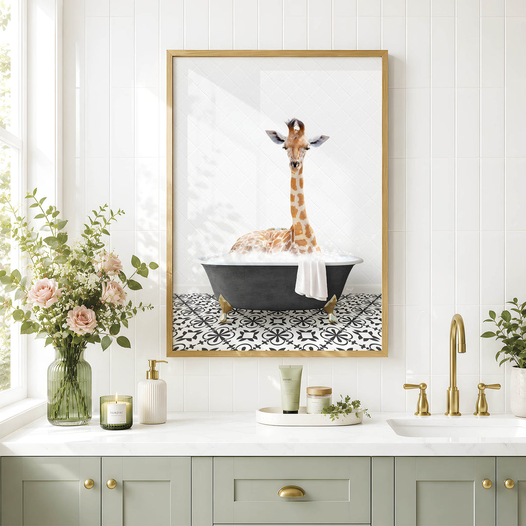 A framed image of a giraffe sitting in a bathtub is displayed on a white tiled wall above a bathroom counter with various toiletries and a vase of flowers.