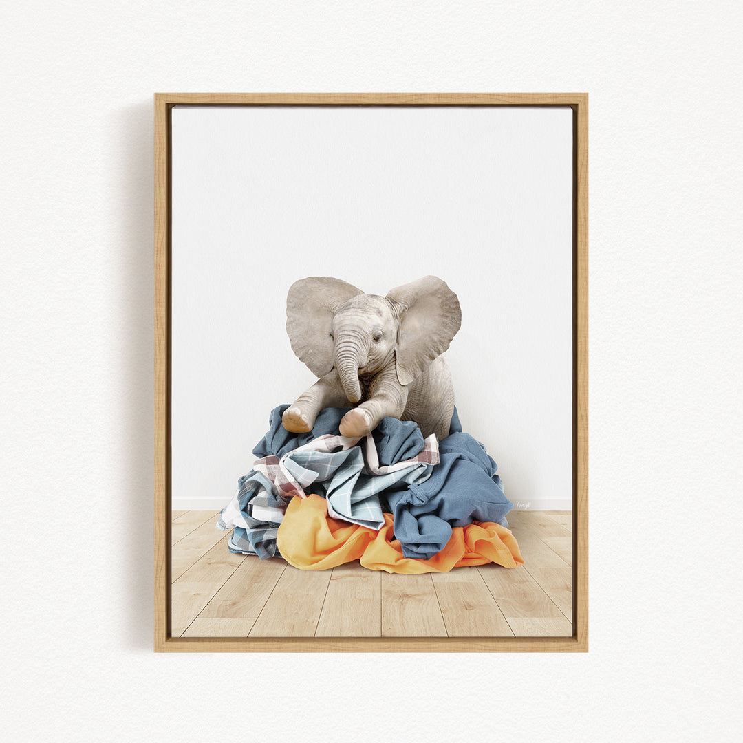 A framed image of a baby elephant sitting on a pile of clothes.