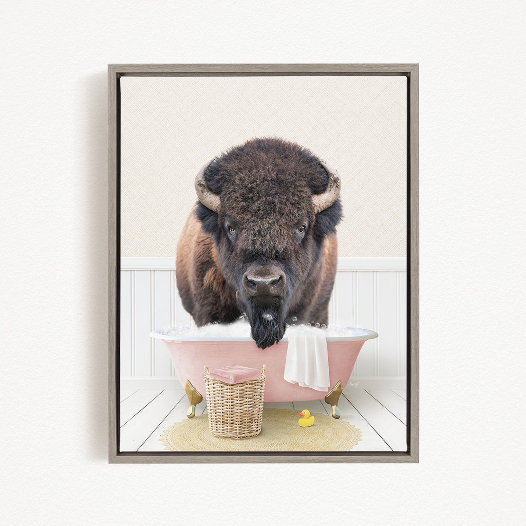 A buffalo with a long, shaggy mane is sitting in a pink bathtub, surrounded by a yellow rubber duck and a wicker basket.