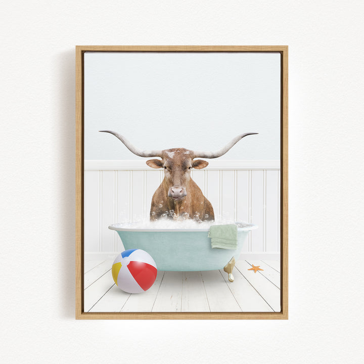 A brown cow with long horns is sitting in a blue bathtub filled with water, surrounded by a beach ball and a towel.