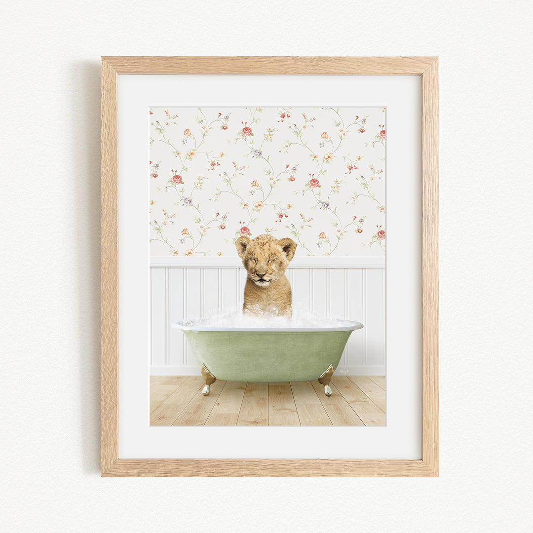 A young lion cub sitting in a green bathtub filled with water, with a floral wallpaper in the background.