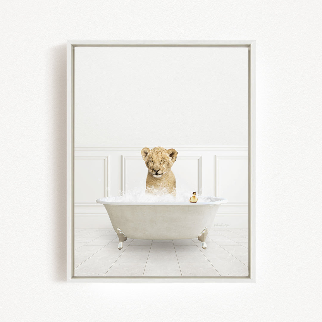 A young lion cub sitting in a white bathtub filled with bubbles, with a small toy animal next to it.