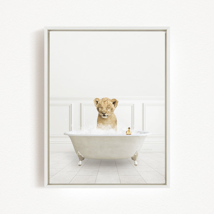 A young lion cub sitting in a white bathtub filled with bubbles, with a small toy animal next to it.
