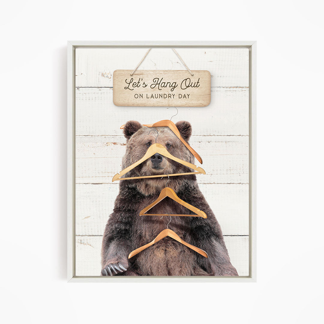 A framed image of a brown bear sitting on a wooden surface, with a sign above it that says "Let's Hang Out on laundry day".