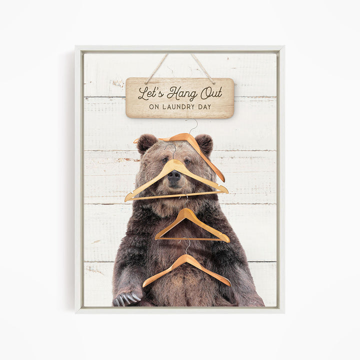 A framed image of a brown bear sitting on a wooden surface, with a sign above it that says "Let's Hang Out on laundry day".