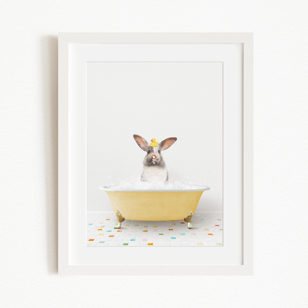 A gray rabbit wearing a yellow hat is sitting in a yellow bathtub filled with bubbles, surrounded by a colorful tiled floor.