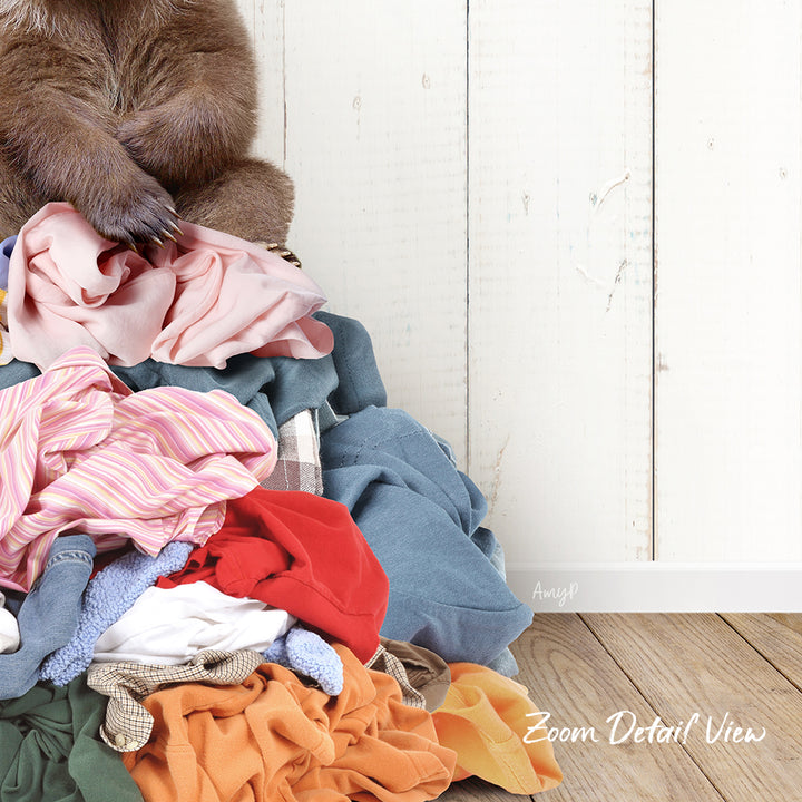A pile of clothes, including various garments and linens, is stacked on a wooden floor against a white wall.