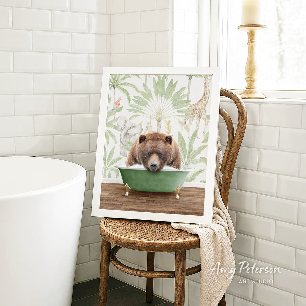 A framed image of a brown bear sitting in a green bathtub, surrounded by tropical foliage, is displayed on a wooden chair in a bathroom setting.