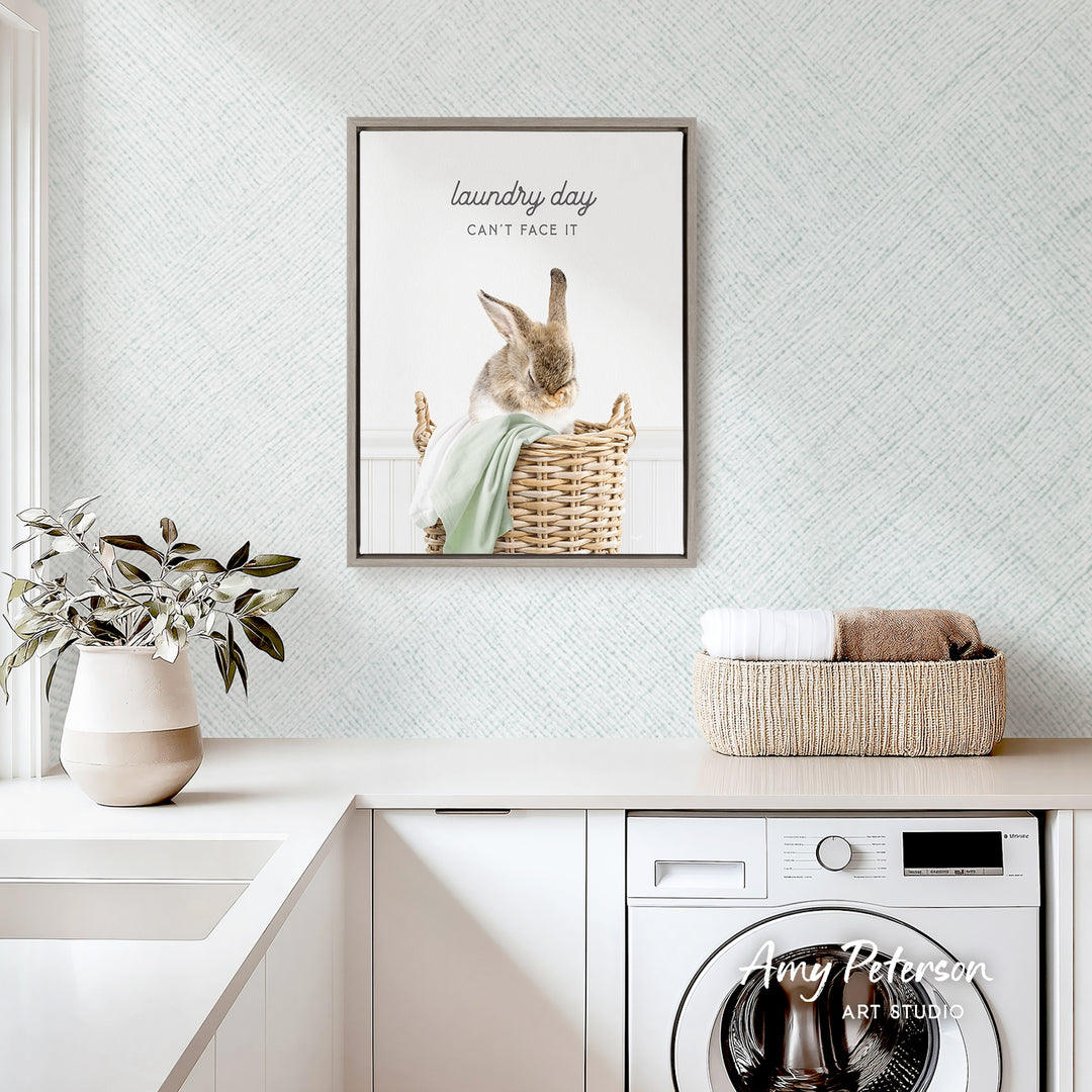 a laundry room with a framed poster of a rabbit in a basket, a potted plant, and a basket of folded towels on a counter.