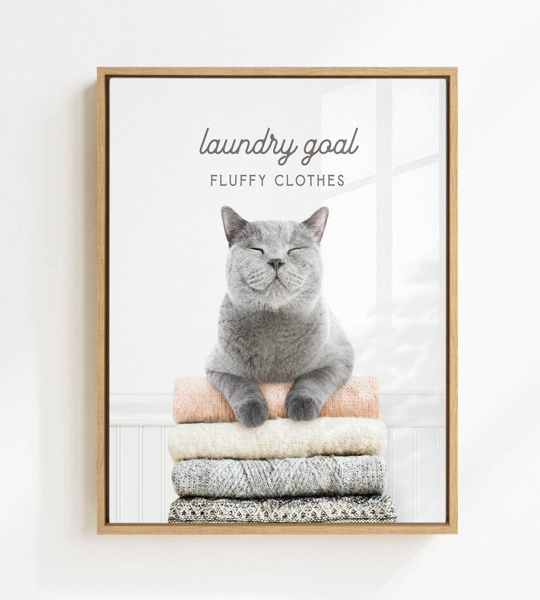 A gray cat sitting on a stack of clothes, with the text "laundry goal FLUFFY CLOTHES" written above it.