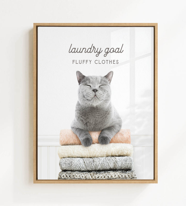 A gray cat sitting on a stack of clothes, with the text "laundry goal FLUFFY CLOTHES" written above it.