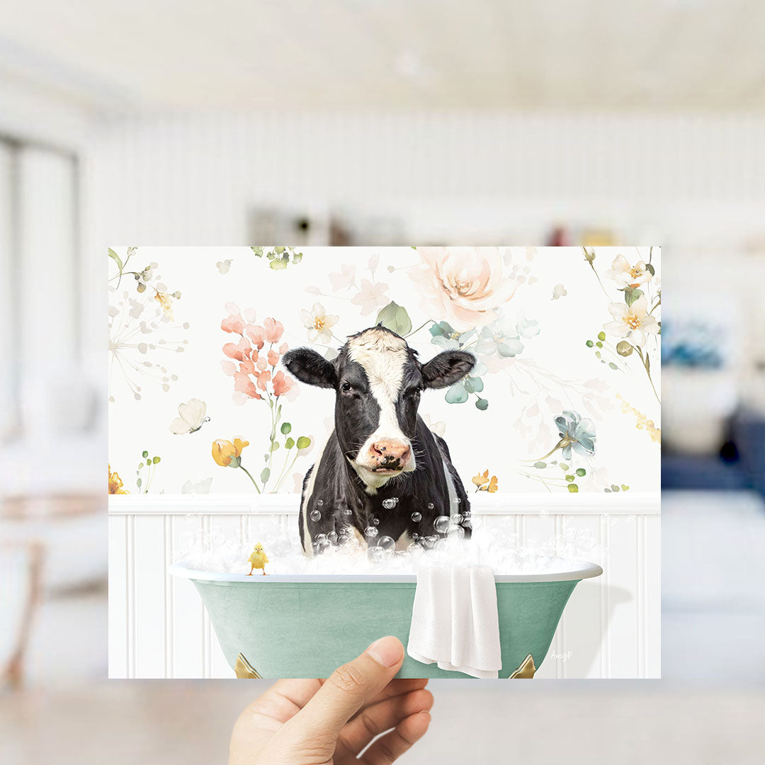 A black and white cow is sitting in a green bathtub filled with bubbles, surrounded by a floral pattern.