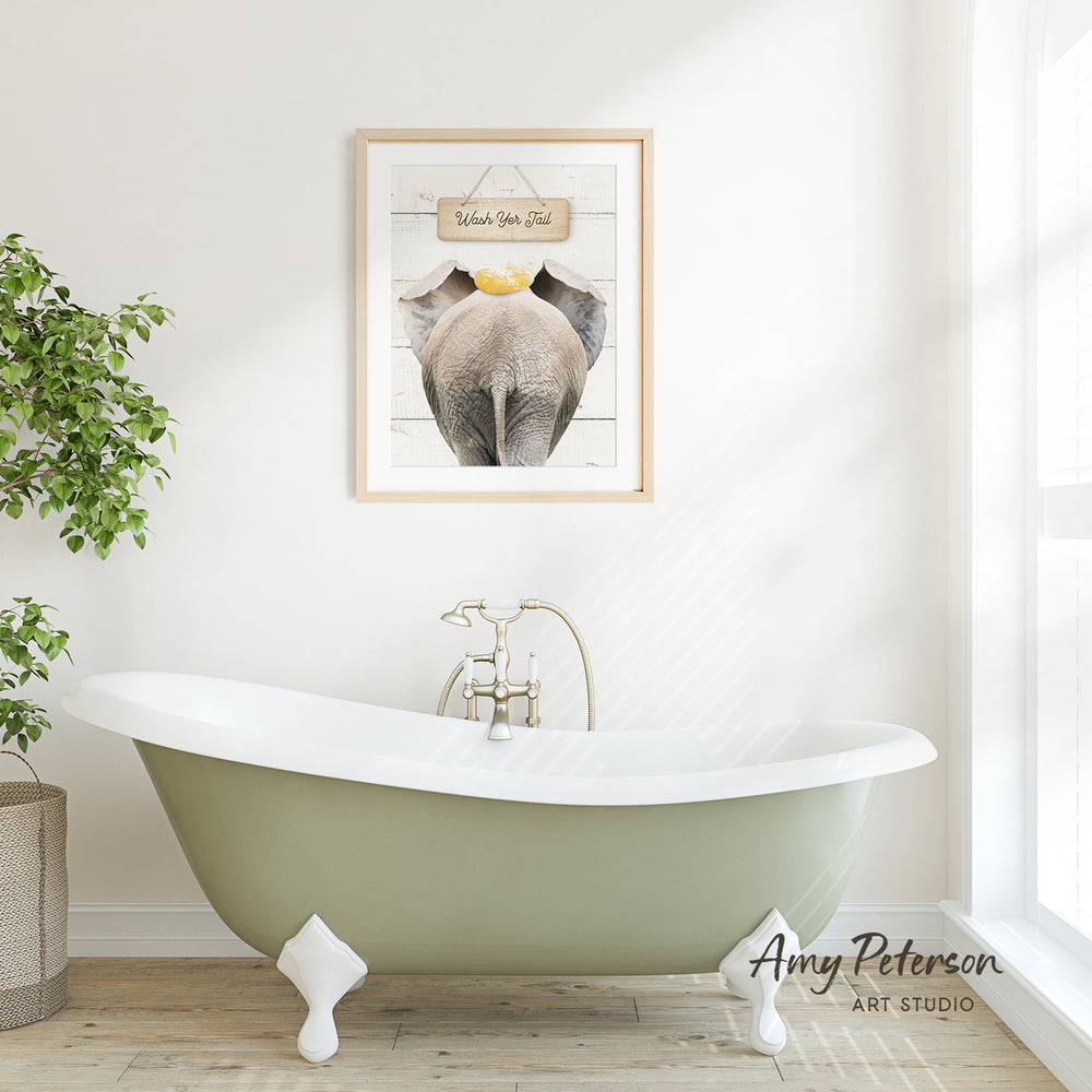 A framed picture of an elephant is hanging on a white wall above a green clawfoot bathtub in a bright, airy bathroom.