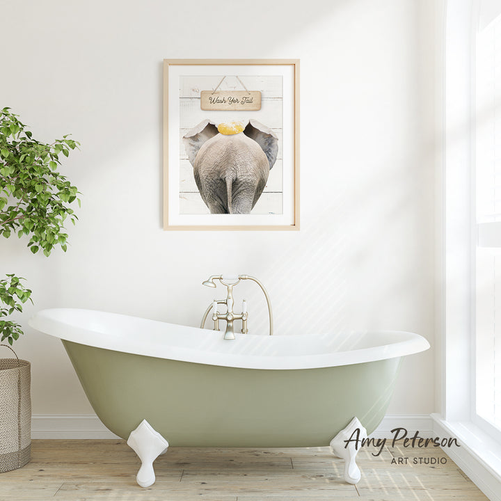 A framed picture of an elephant is hanging on a white wall above a green clawfoot bathtub in a bright, airy bathroom.