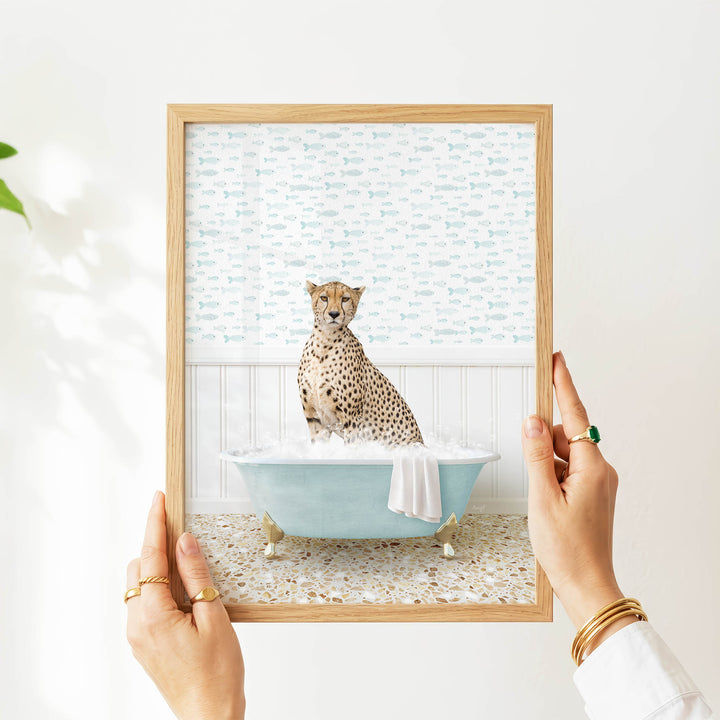 A person's hands are holding a framed picture of a cheetah sitting in a bathtub filled with water, surrounded by a pattern of fish.