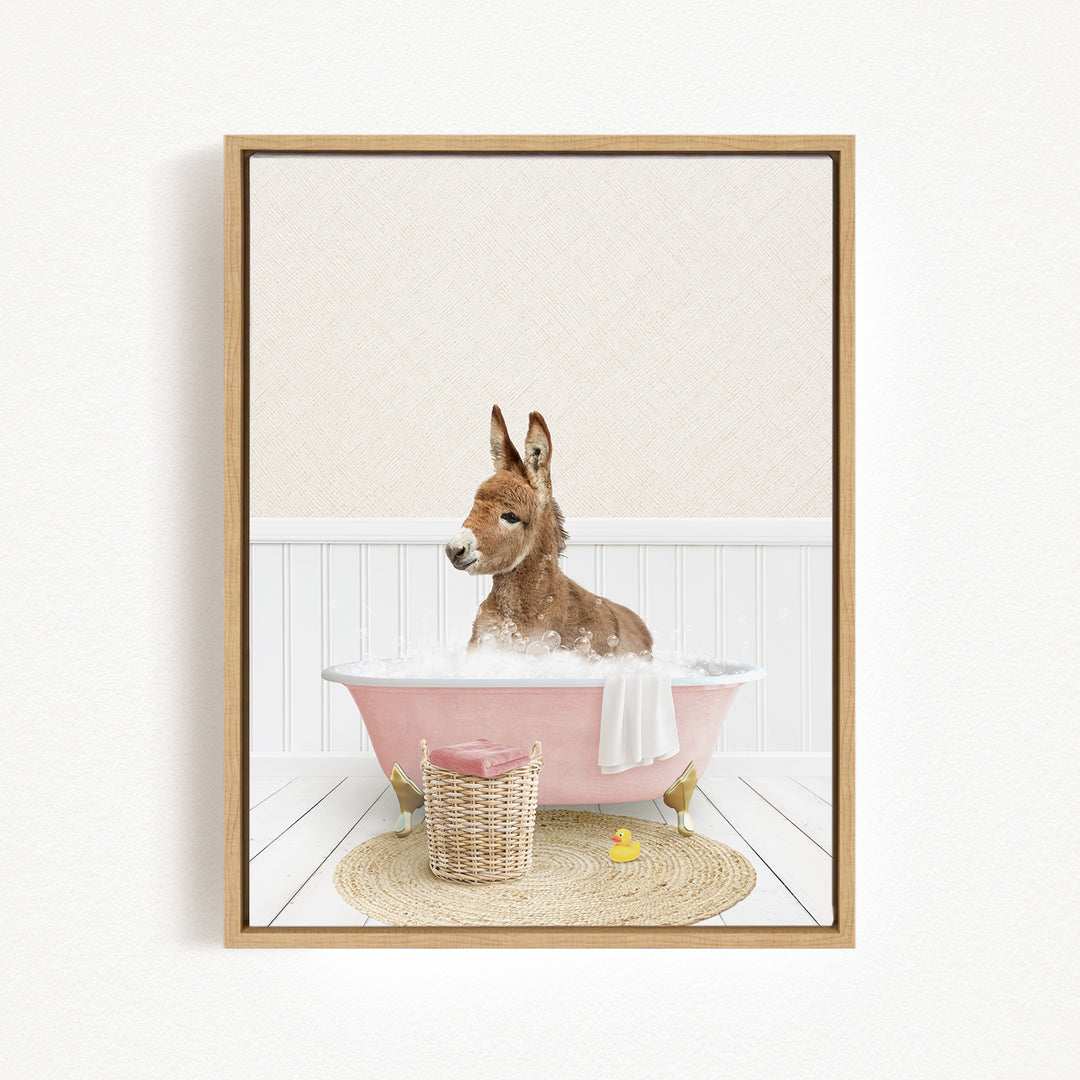 A donkey is sitting in a pink bathtub filled with bubbles, surrounded by a basket of toys and a yellow rubber duck.