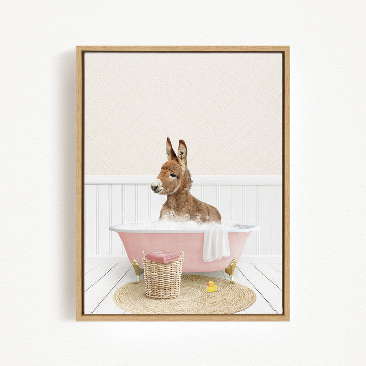 A donkey is sitting in a pink bathtub filled with bubbles, surrounded by a basket of toys and a yellow rubber duck.
