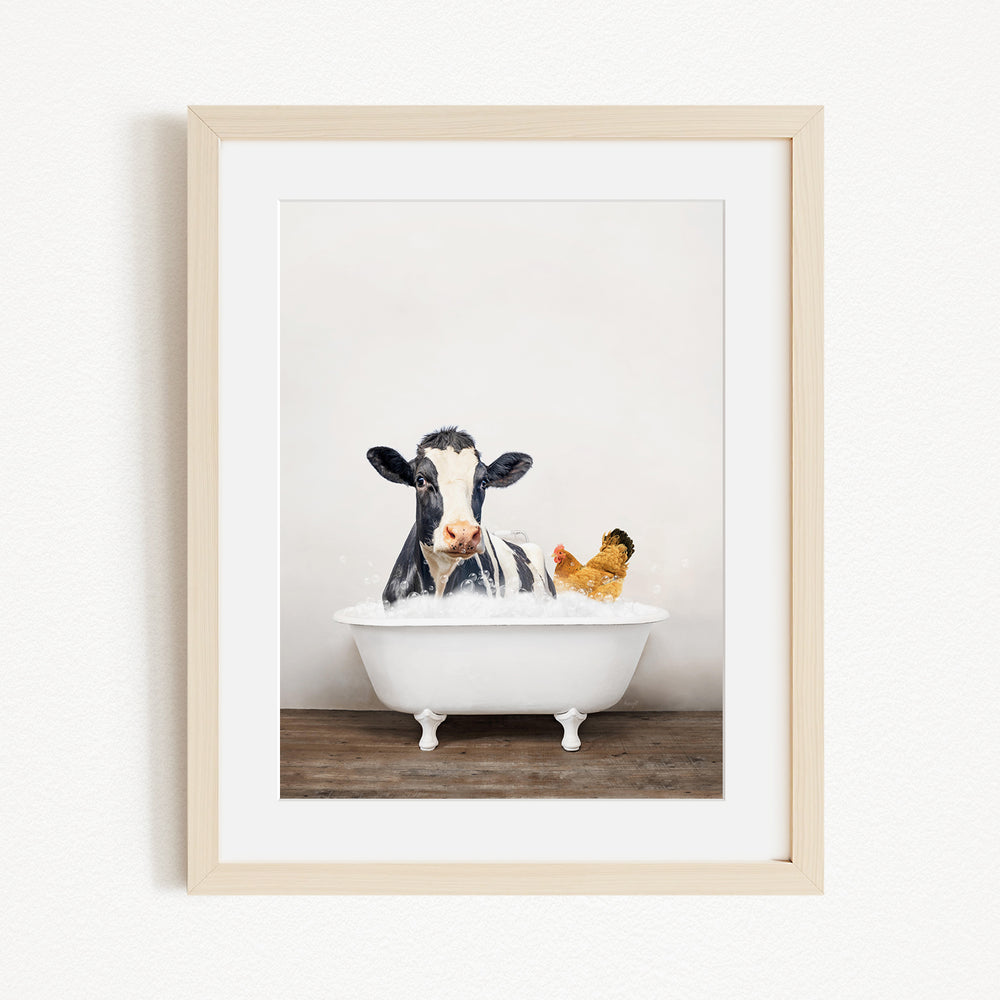 A framed image depicting a cow sitting in a bathtub, with a chicken nearby, creating a whimsical and humorous scene.