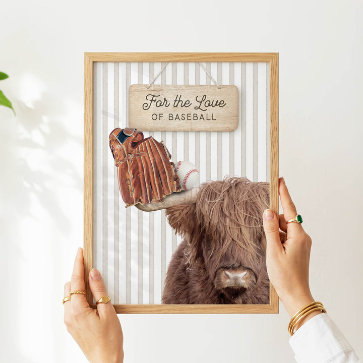 A person's hands are holding a framed picture of a cow with baseball gloves on its head, and a sign that says "Far the Love of Baseball".