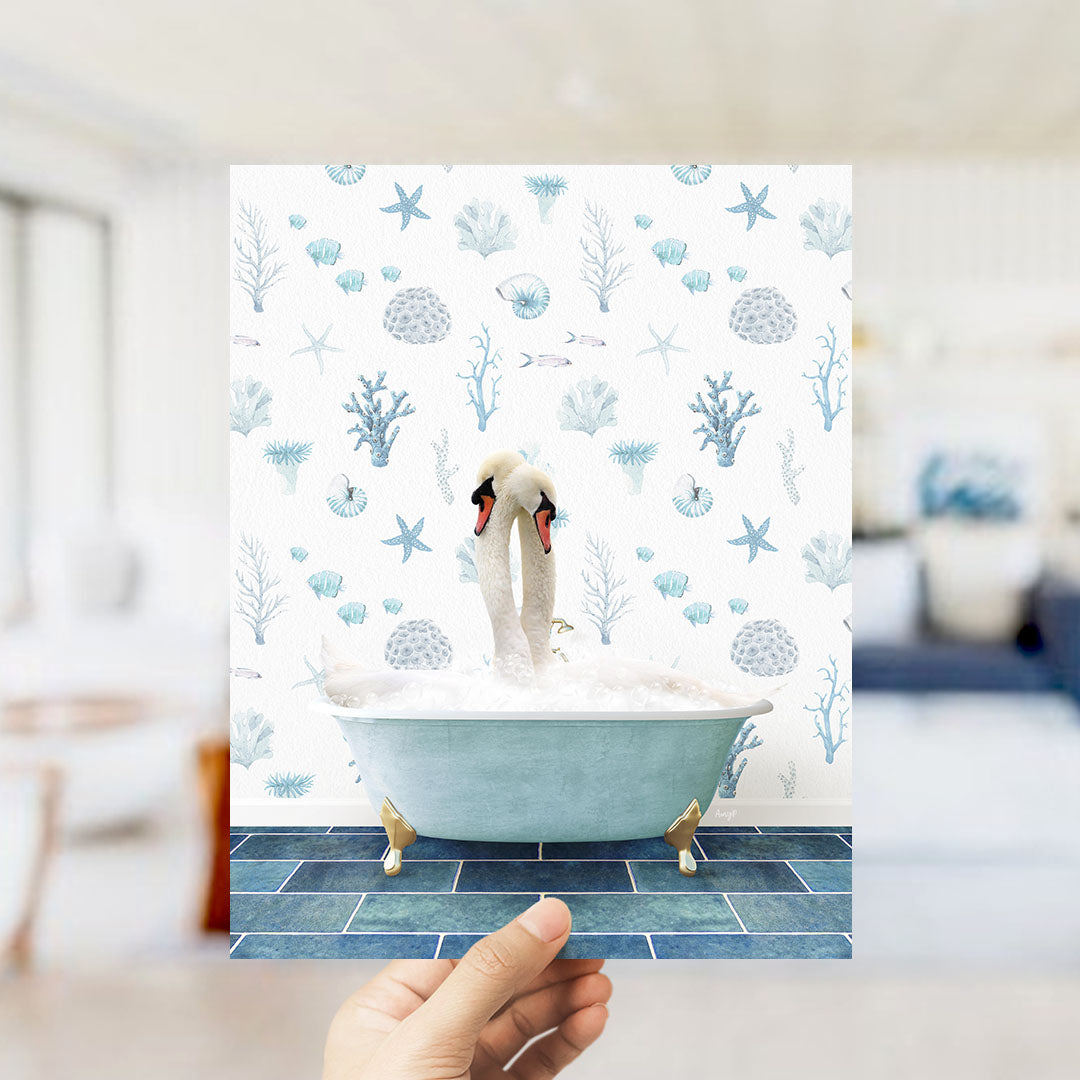 A hand holds up a printed image of two swans sitting in a bathtub filled with bubbles, surrounded by a pattern of seashells, starfish, and other marine life.
