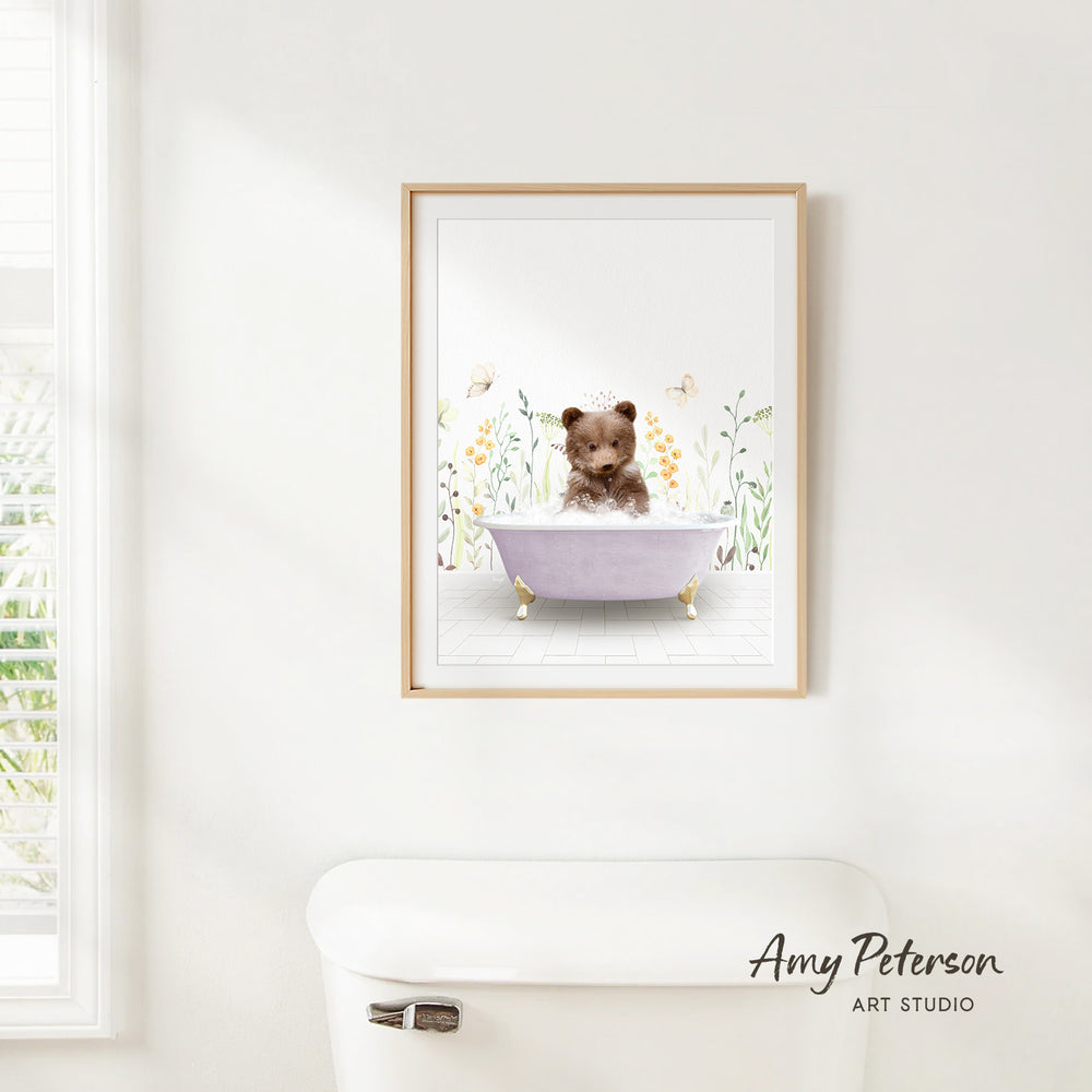 A framed illustration of a bear sitting in a bathtub surrounded by flowers and butterflies is hanging on a white wall.