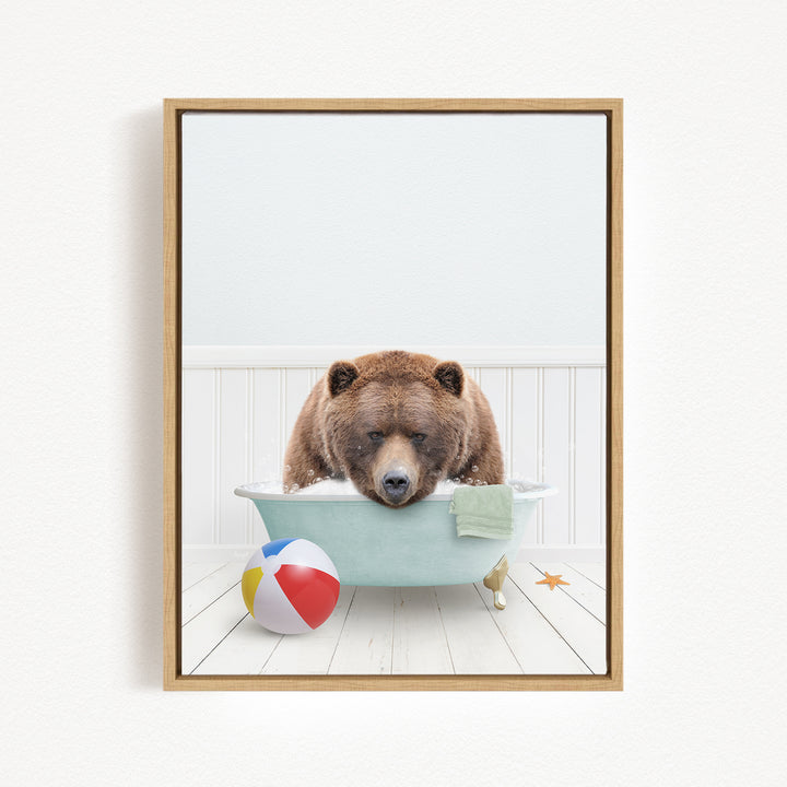 A brown bear is sitting in a bathtub filled with water, surrounded by a beach ball and a towel.