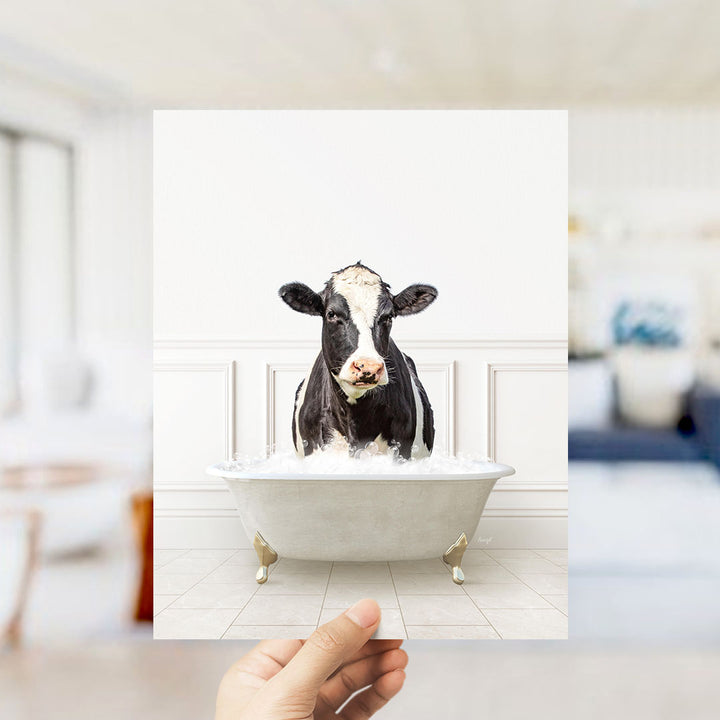 A black and white cow is sitting in a white bathtub filled with water, appearing to be enjoying a bath.