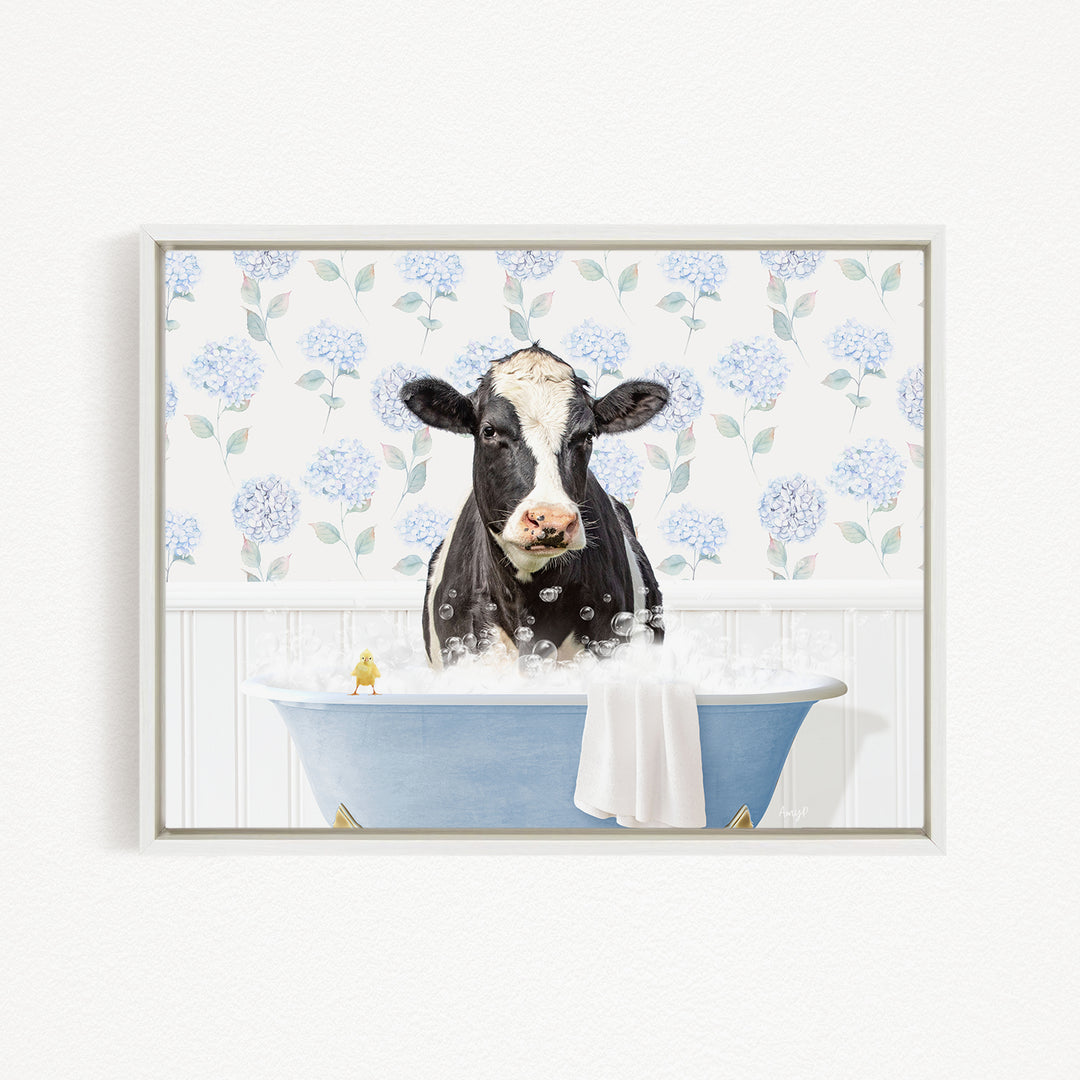 A black and white cow is sitting in a blue bathtub filled with bubbles, with a small yellow bird perched on the edge of the tub.