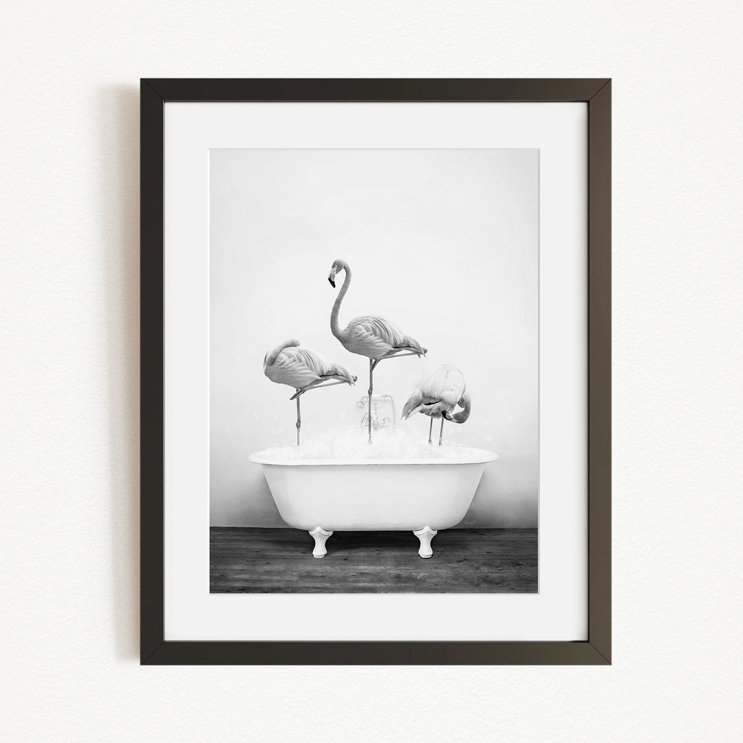 A black and white photograph of three flamingos standing in a white bathtub filled with water.