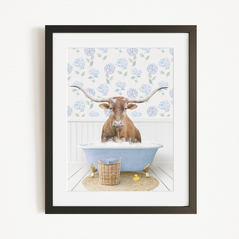 A brown cow with large horns is sitting in a blue bathtub filled with water, surrounded by a floral patterned wall and a basket of rubber ducks.
