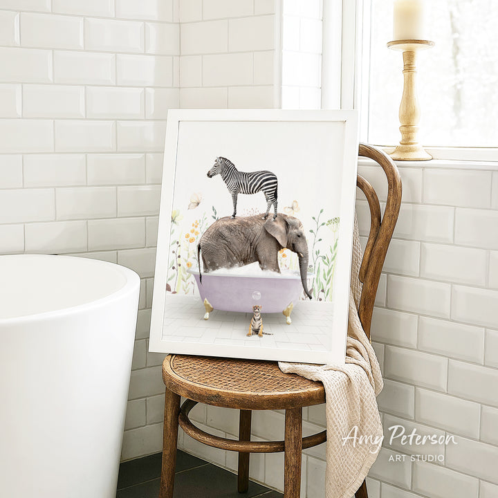 A framed illustration of a zebra standing on an elephant in a bathtub, surrounded by flowers, is displayed on a wooden chair in a bathroom setting.