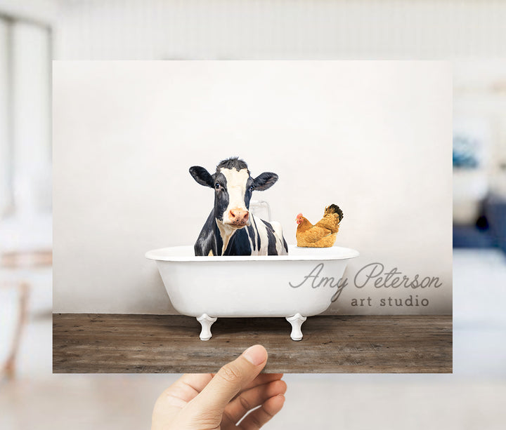 a hand holding up a card with a picture of a cow in a bathtub