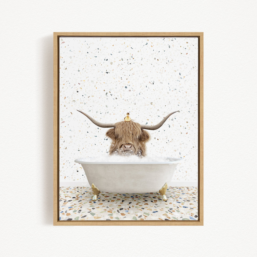 A framed image depicting a cow with long horns sitting in a bathtub filled with bubbles, with a bird perched on its head.