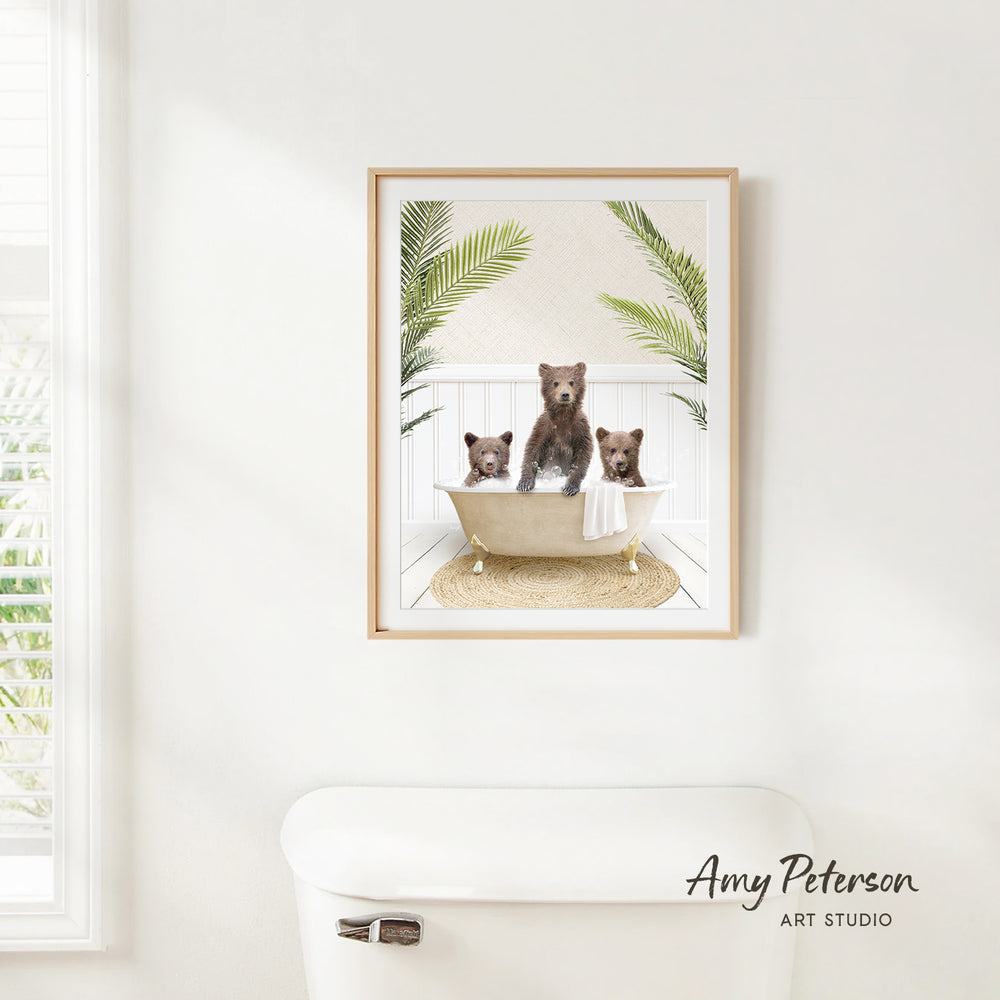 A framed image of three bears sitting in a bathtub, surrounded by palm leaves, is hanging on a white wall.